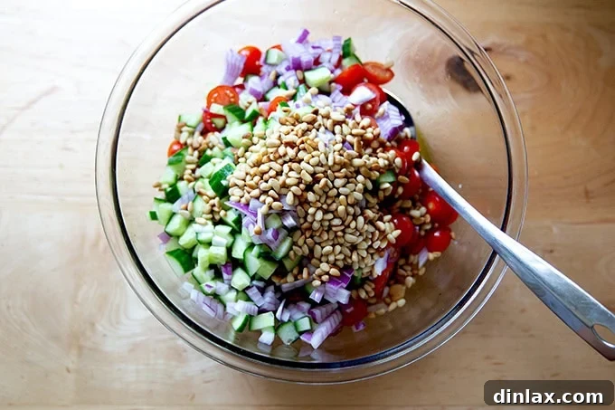 A large bowl filled with chickpeas, vibrant halved cherry tomatoes, crisp diced cucumber, finely chopped red onion, and golden toasted pine nuts, all tossed in the lemon vinaigrette.