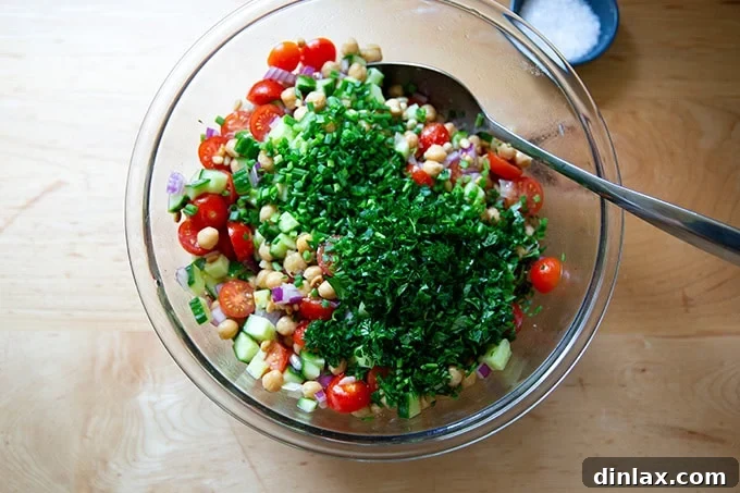 The herby chickpea salad in a large bowl, now enriched with generous amounts of freshly chopped chives and parsley, completing the fresh flavor profile.