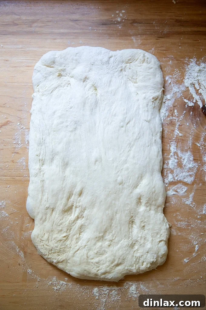 Sourdough discard toasting bread dough skillfully stretched out on a work surface, forming a large, even rectangle.