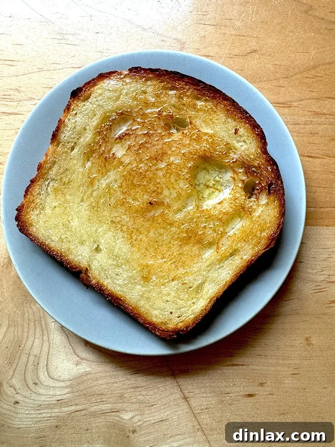 A perfectly toasted and buttered slice of sourdough discard toasting bread, presented on a plate, highlighting its golden crust and inviting texture.