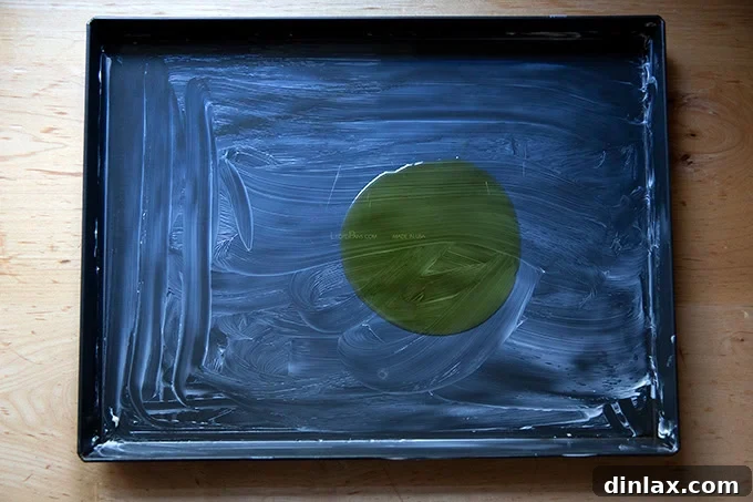 A shiny Lloyd grandma-style pizza pan, meticulously buttered across its surface and featuring a generous drizzle of 1 tablespoon of olive oil in its center, prepared for dough.