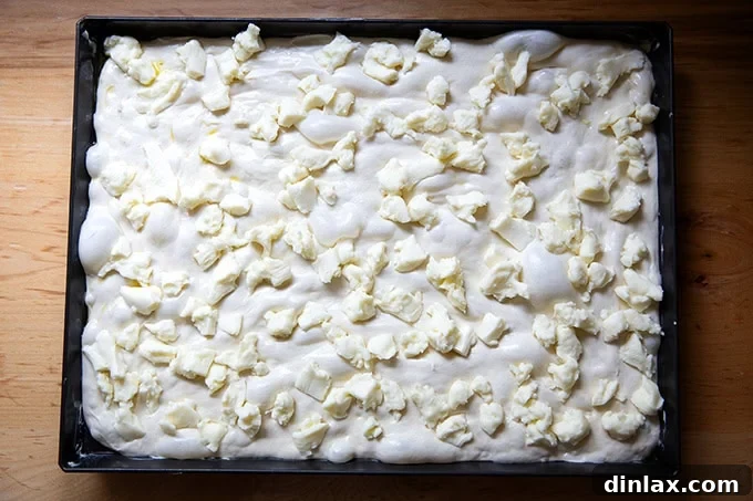 The stretched Grandma-style pizza dough, generously covered with an even layer of shredded mozzarella cheese, extending to the pan's edges, ready for additional toppings.