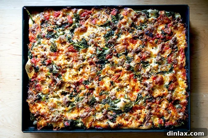 A just-baked Grandma-style pizza, still in its pan, showcasing a perfectly golden and caramelized crust, topped with sausage, broccoli rabe, melted mozzarella, and a hint of calabrian chile-spiked tomato sauce.