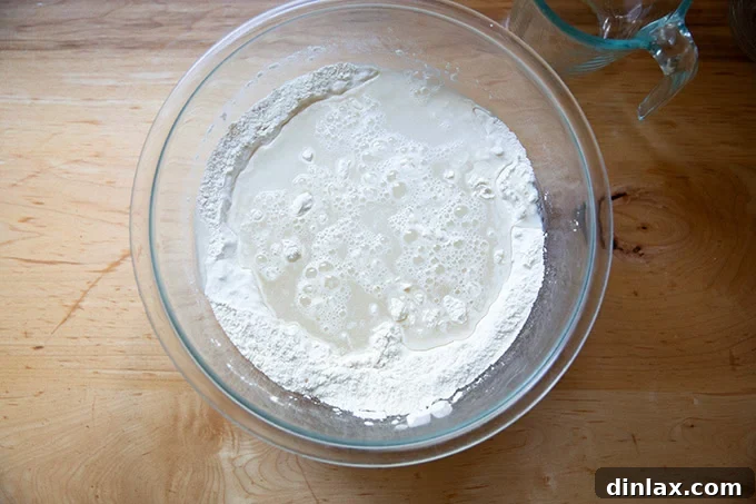 Clear water being poured into a bowl containing the dry ingredients of flour, salt, and yeast, poised for mixing into focaccia dough.