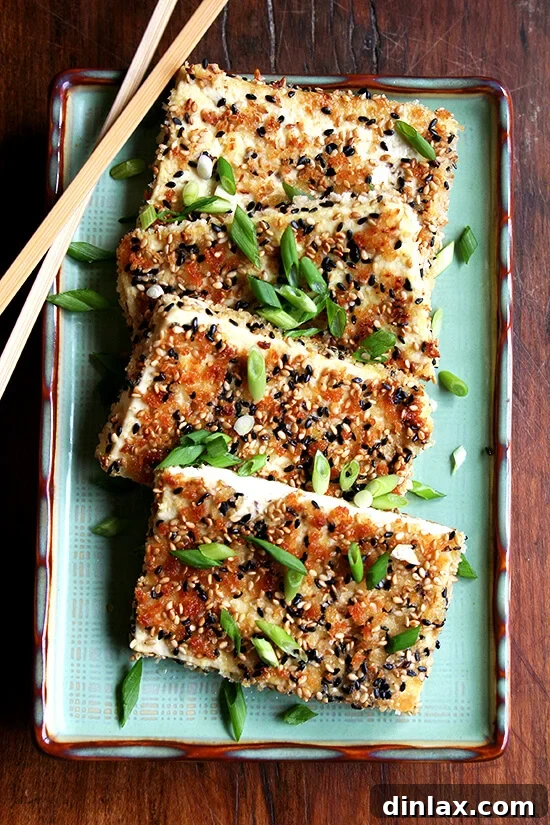 Golden Sesame Tofu with Tangy Nuoc Cham Drizzle 6 pan-fried sesame-crusted tofu on a platter, golden brown and perfectly crispy, ready to be served.
