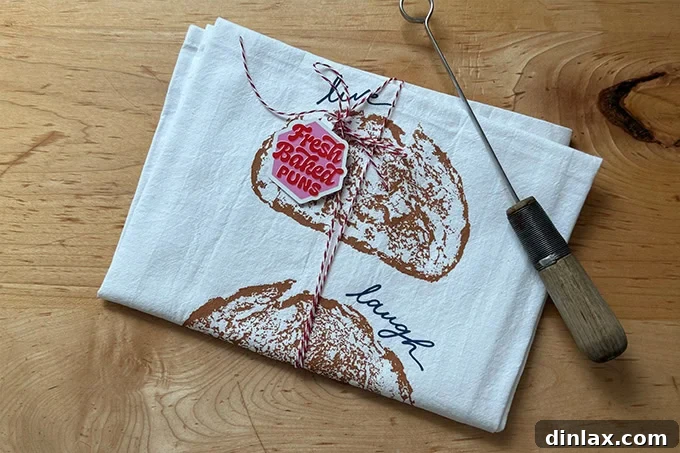 A charming 'Live Laugh Loaf' printed tea towel, folded to display its clever food pun design, ideal for the sourdough baker.