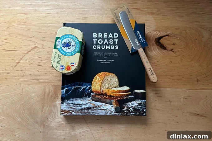 The 'Bread Toast Crumbs' cookbook open on a page, with an elegant Opinel butter spreader and a block of gourmet French butter beside it, suggesting a delightful culinary experience.