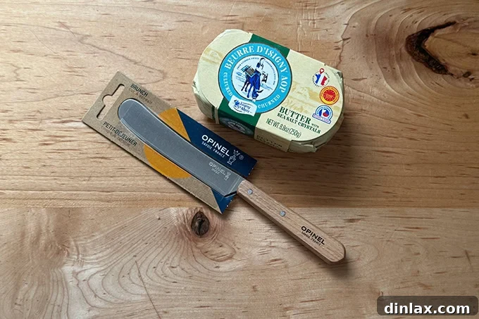 A close-up of a stylish Opinel butter spreader resting beside a luxurious block of gourmet French butter, ready for enjoying with freshly baked bread.