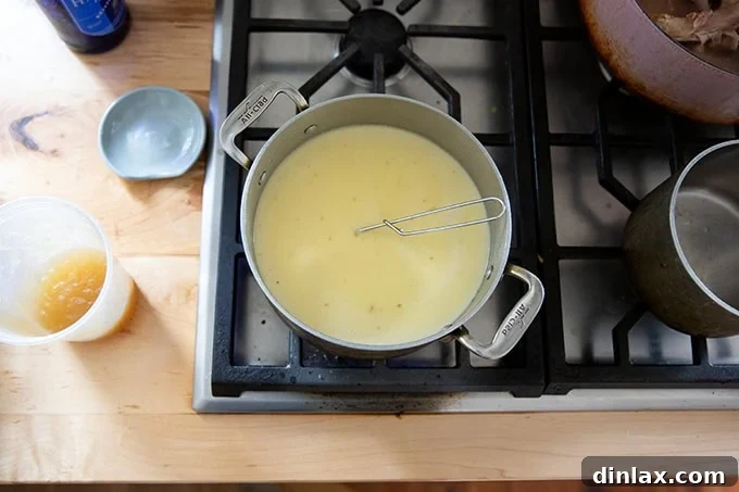 A large pot on the stovetop simmering the creamy, stock-based sauce for Turkey Tetrazzini, showing a smooth and slightly thickened consistency.