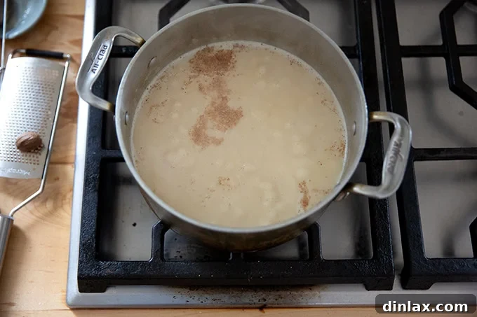 The simmering sauce for turkey tetrazzini, showing a fine grating of fresh nutmeg being added, enhancing its aromatic profile.