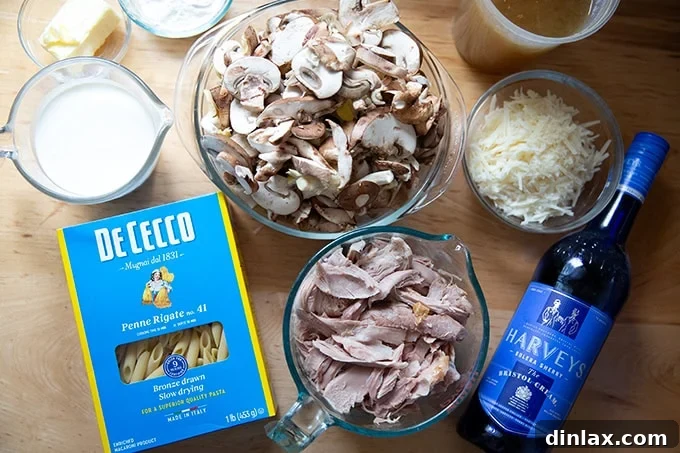 Various ingredients for turkey tetrazzini, including pasta, mushrooms, turkey, stock, and cream, neatly arranged on a kitchen countertop.