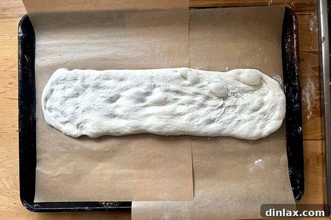 Giant sandwich roll dough stretched into a log on an extra-large parchment-lined sheet pan.
