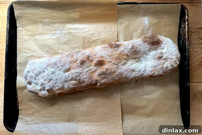 Just-baked giant sandwich roll on a parchment-lined sheet pan.