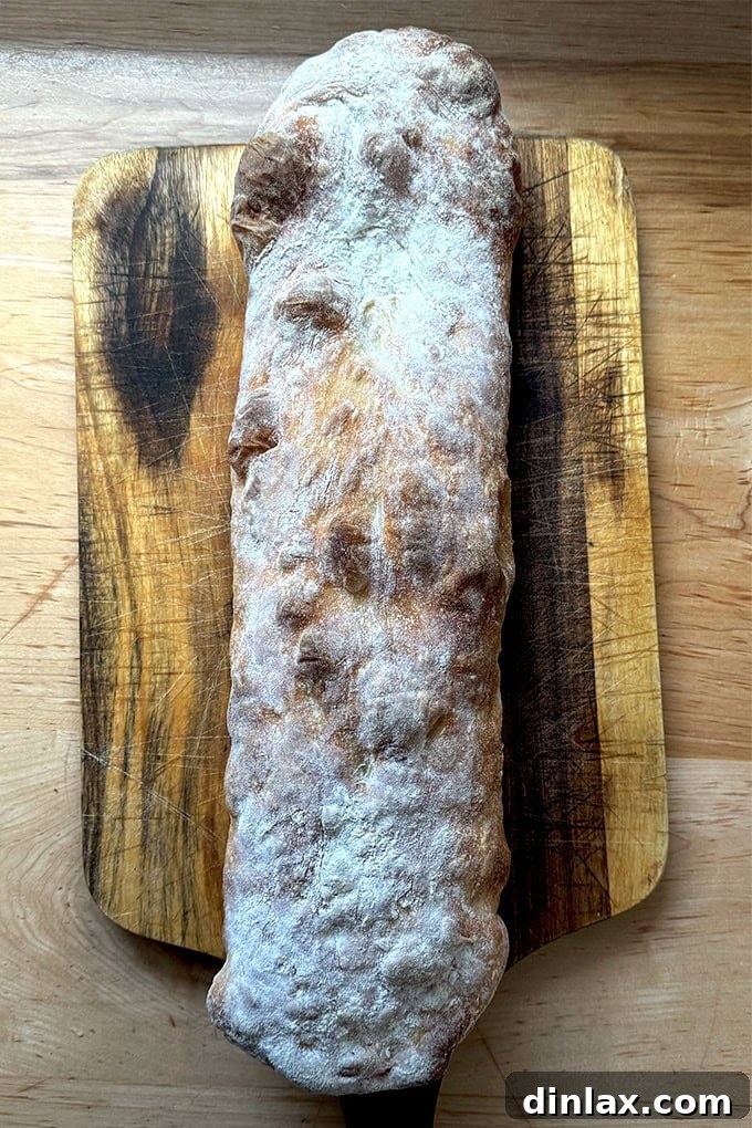 A just-baked giant sandwich roll on a cutting board.