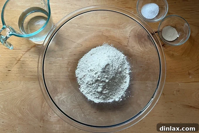 The ingredients to make a giant overnight sandwich roll on a countertop: flour, water, salt, yeast.