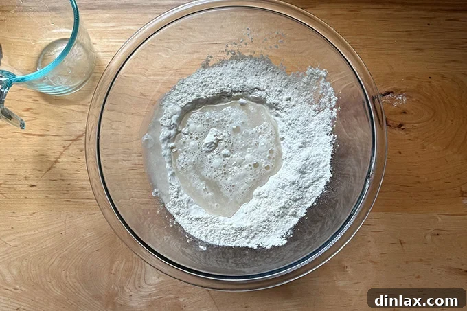 Water added to the dry ingredients to make sandwich roll dough in a large glass bowl.
