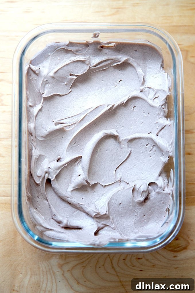 A glass storage container holding a generous amount of chocolate whipped cream cheese frosting, ready for refrigeration.