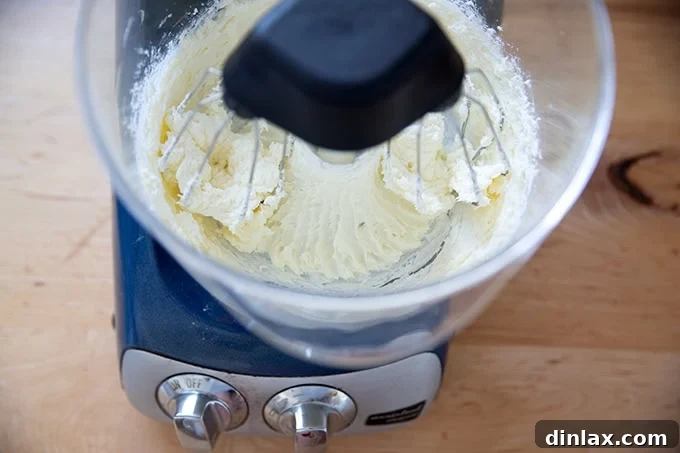 A stand mixer beating together sugar and cream cheese, showing the mixture becoming light and fluffy.