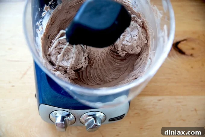 A stand mixer actively beating together all the ingredients for chocolate cream cheese frosting, showing it come together.