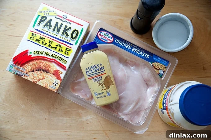 The ingredients to make chicken cutlets on a countertop: panko bread crumbs, thinly sliced chicken breasts, mustard, mayonnaise, salt, and pepper.
