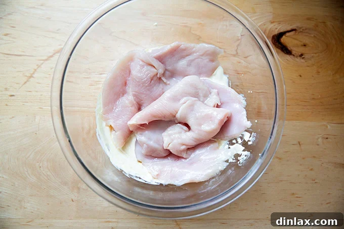 Chicken cutlet in a bowl filled with a mayonnaise-mustard mixture.
