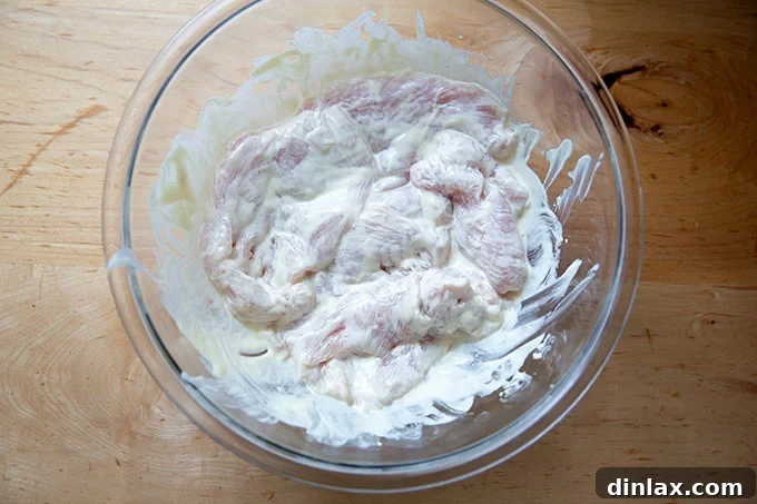 A large bowl filled with chicken cutlets coated in a mayonnaise mustard mixture.