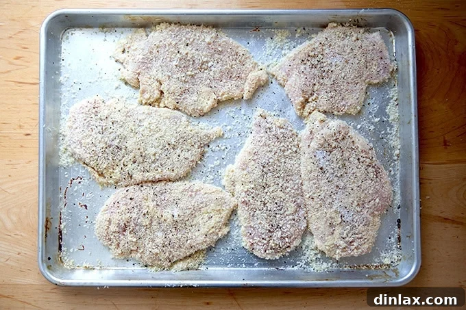 Six breaded uncooked chicken cutlets on a sheet pan.