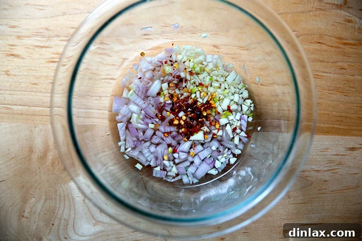 Zesty Homemade Chimichurri 4 Finely minced shallots, garlic, and crushed red pepper flakes mixed with white balsamic vinegar and salt in a bowl.