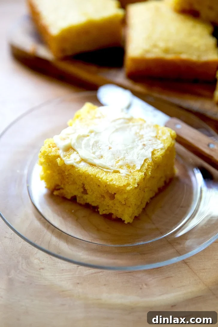 A piece of cornbread, spread with butter, on a small glass plate.