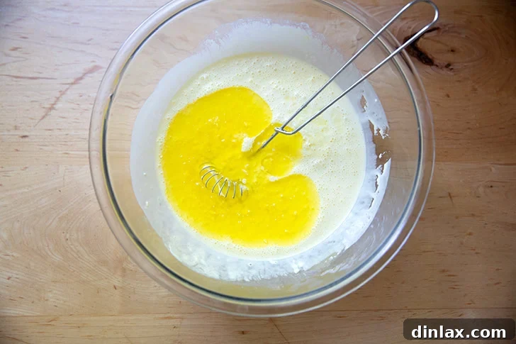 Melted butter added to the wet ingredients to make cornbread in a large bowl.